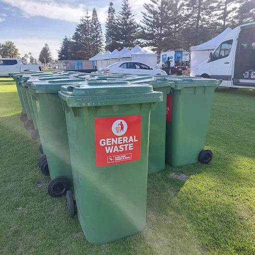 A row of Adelaide Wheelie Bins 240 litre general waste bins standing on the grass at an outdoor event